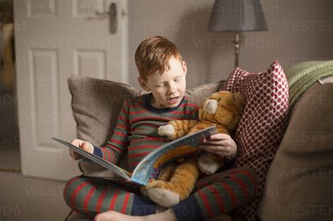 Boy reading a book on couch at home stock photo