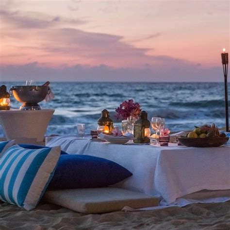 a table set up on the beach with candles and food in front of it,