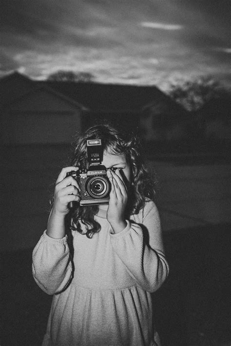 A girl holding a camera in a black and white photo with flash.