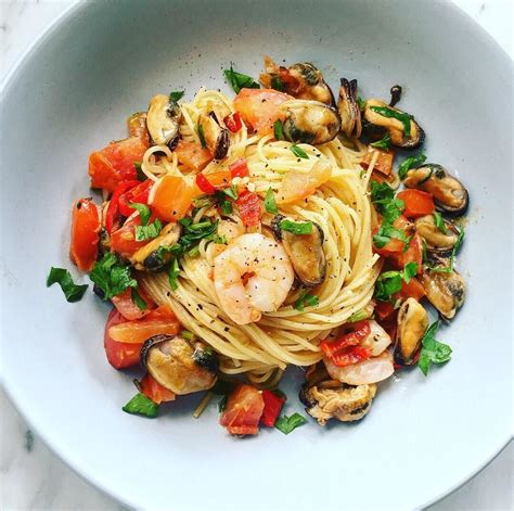 a white bowl filled with pasta, shrimp and veggies on top of a marble table