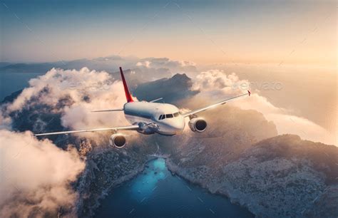 White airplane is flying over mountains and low clouds Stock Photo by den-belitsky