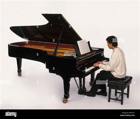 Teenage boy playing grand piano, reading from sheet music, side view Stock Photo - Alamy