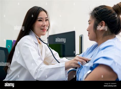 Smiling Asian female doctor cardiologist examining fat woman cardiac patient listening checking ...