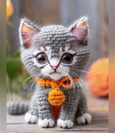 a small crocheted kitten wearing a yellow and orange necktie sitting on ...