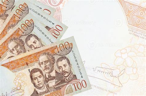 100 Dominican peso bills lies in stack on background of big semi-transparent banknote. Abstract ...