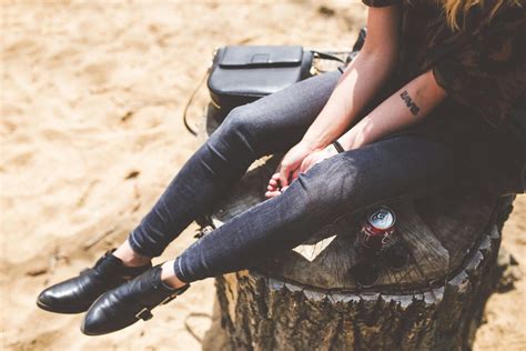 Woman Wearing Black Jacket Blue Distressed Jeans and Brown Boots Sitting on Gray Concrete ...