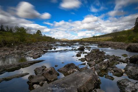 a river running through a lush green forest under a blue sky with white ...