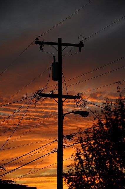 the sun is setting behind power lines and telephone poles, with trees ...