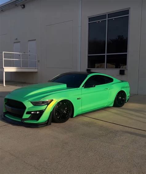 a bright green mustang parked in front of a white building with black wheels and rims