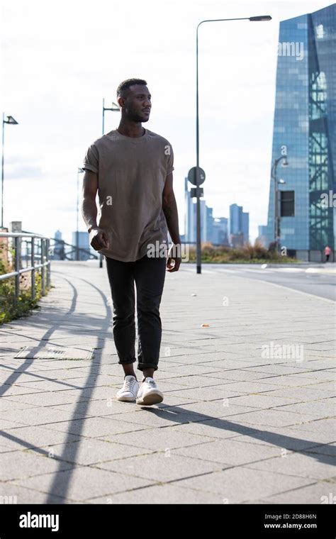 Young black man walking on sidewalk. Head turned, looking away. Full ...