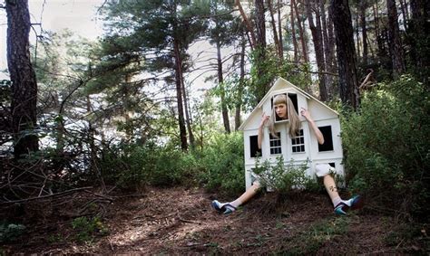 a woman is sitting in a small white house surrounded by trees and bushes, with her hands on her head