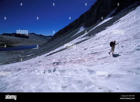 A backpacker hiking up a snow covered slope in Eastern Sierra Nevada ...