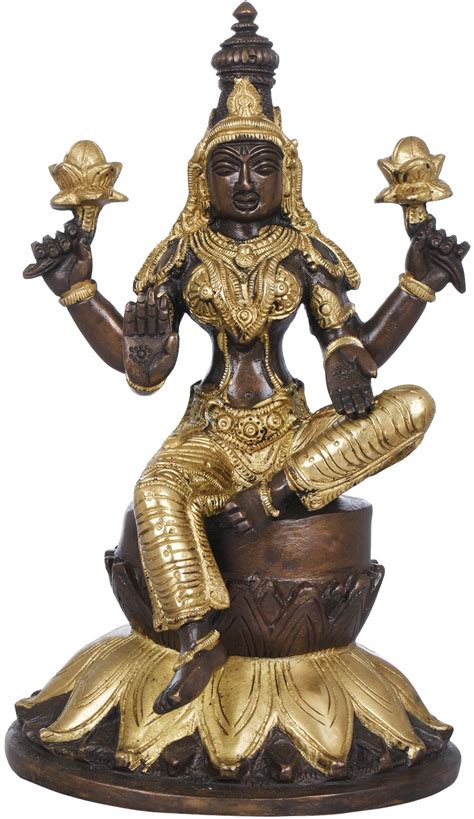 a golden statue sitting on top of a wooden bowl filled with gold colored items and holding two