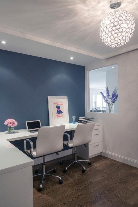 This modern home office features a white desk with two white leather desk chairs positioned in ...