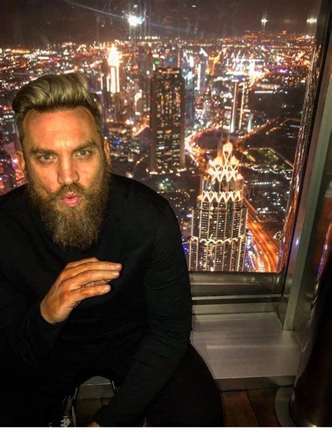 a man with a beard sitting in front of a window looking out at the city