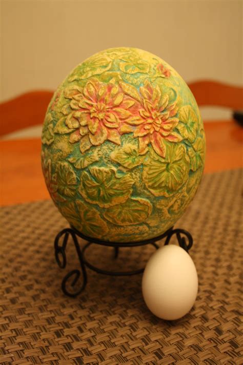 an egg sitting on top of a stand next to a white ball with flowers painted on it