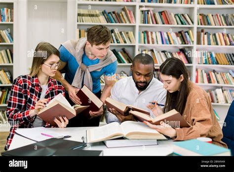 Smart confident young multiethnical students reading books at the table ...