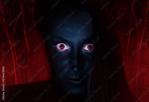 Scary face of a witch with dark skin and red eyes staring, with burning ...