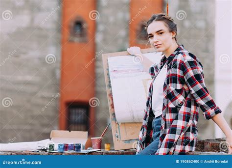 Woman Artist Paints a Picture while Sitting on a Brick Wall on a Background of Old Architecture ...