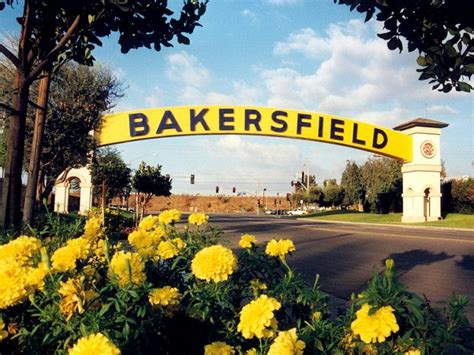 a yellow sign that says bakersfield on the side of a road with flowers ...