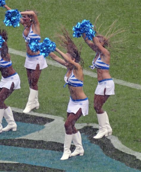 cheerleaders perform on the sidelines during a football game in the rain with blue pom - poms