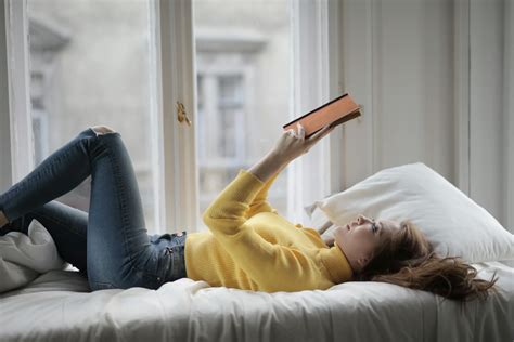 Woman in Yellow Sweater Lying on Bed While Reading Book · Free Stock Photo