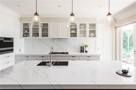 a large white kitchen with marble counter tops and an island in front of glass doors