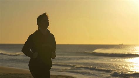 Person jogging exercising by beach with sun behind slowmo Stock Video Footage - Storyblocks