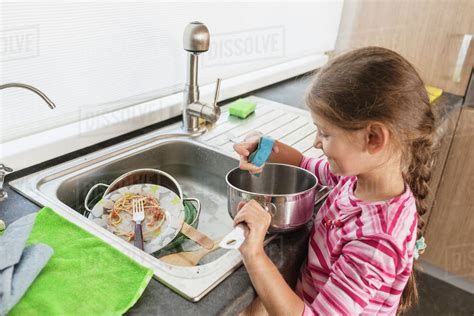 Smiling girl washing dishes at kitchen sink - Stock Photo - Dissolve