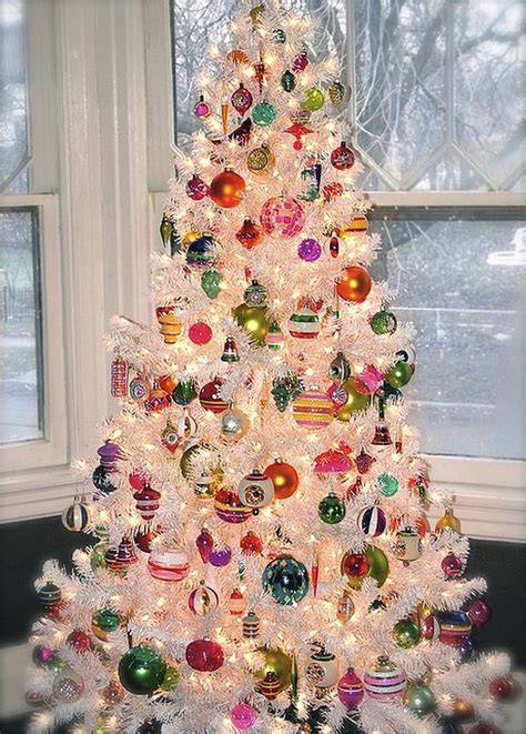 a white christmas tree with colorful ornaments in front of a window and snow covered ground