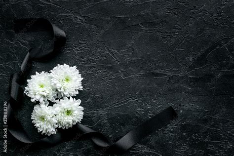 Funeral symbols. White flower near black ribbon on black background top view space for text ...