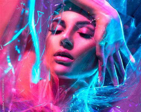 Fashion model woman in colorful bright neon lights posing in studio through transparent film ...