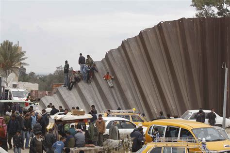 Palestinians cross over a section of the border wall separating the ...