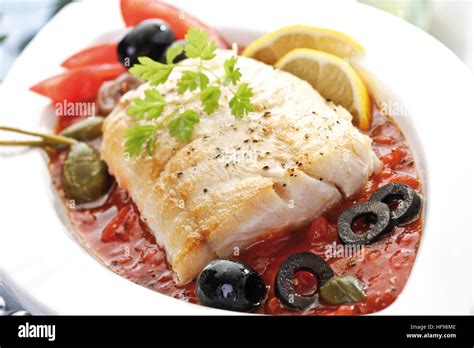 Mediterranean seafood dish: fried Victoria Sea Bass with tomato sauce, black and green olives ...