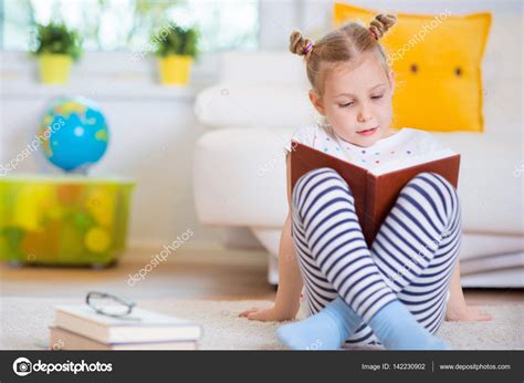 Portrait of clever little girl sitting with book on the floor Stock ...