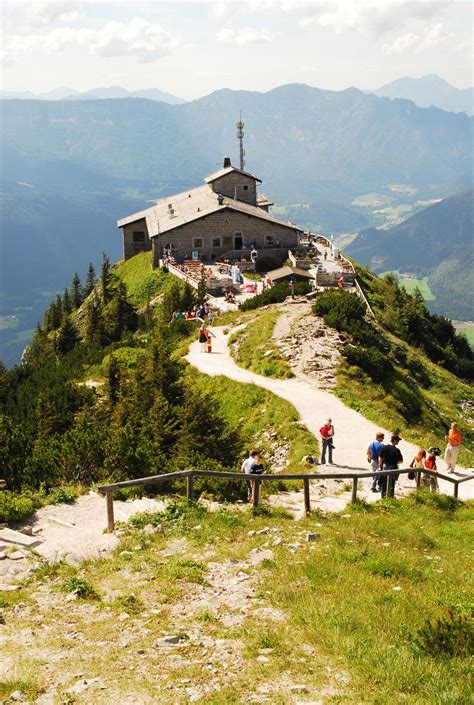 people standing at the top of a mountain looking down on a small building with a steep slope