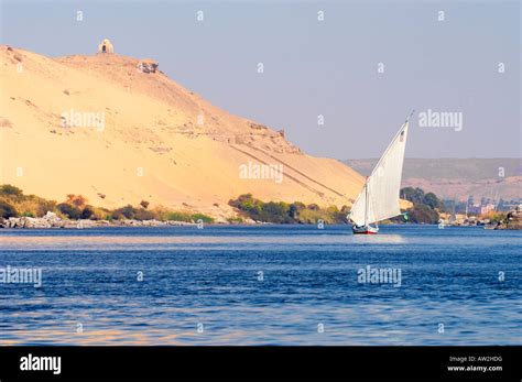 Felucca glides along behind Kitchener's Island, Aswan, Egypt. Tombs of the Nobles in the cliffs ...