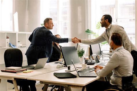 Businessmen shaking hands during sales meeting in office stock photo