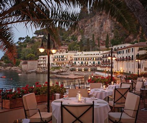 an outdoor dining area with tables and chairs next to the water at dusk ...