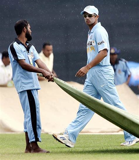 Rahul Dravid walks past a groundsman handling the covers as it begins ...