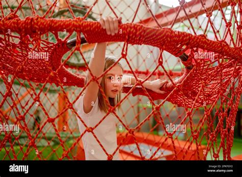 Pretty child girl in net in amusement park having fun. Happy preteen kid enjoying entertainment ...