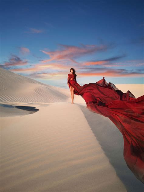 a woman in a red dress is walking through the sand dunes at sunset or dawn