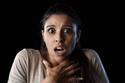 young beautiful scared Spanish woman in shock and surprise face expression isolated on black ...