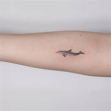 Fine line dolphin tattoo on the right inner forearm.