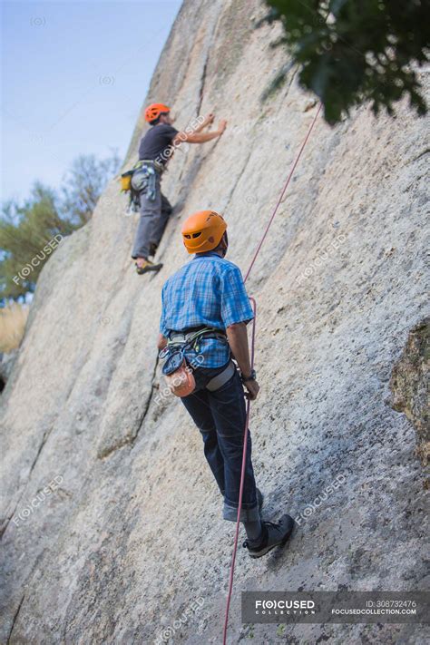 Adventurers climbing mountain wearing safety harness against ...