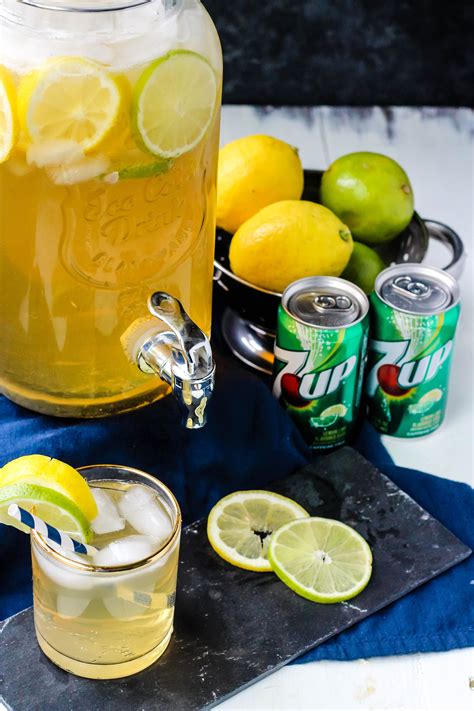 a pitcher of lemonade next to two cans of soda and limes on a table