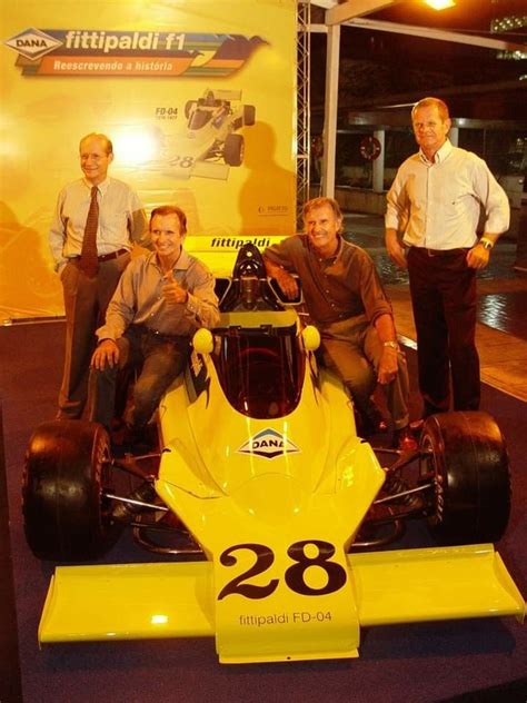 three men standing next to a yellow race car in front of a sign with the number 28 on it