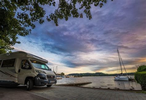 an rv parked next to the water with boats in the background at sunset ...