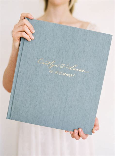 a woman holding up a blue book with gold writing on it's front cover