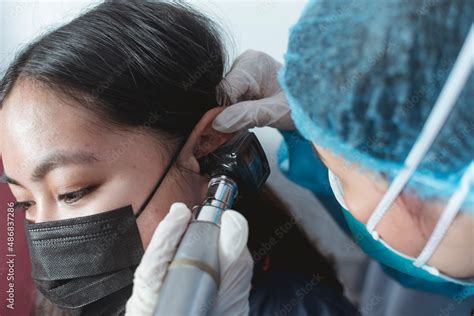 A doctor in full PPE gear checks the ear drum of a female patient with ...